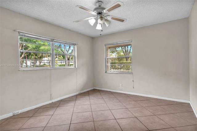 empty room featuring ceiling fan, light tile patterned floors, a textured ceiling, and baseboards