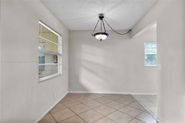 unfurnished dining area with a textured ceiling, light tile patterned floors, and baseboards