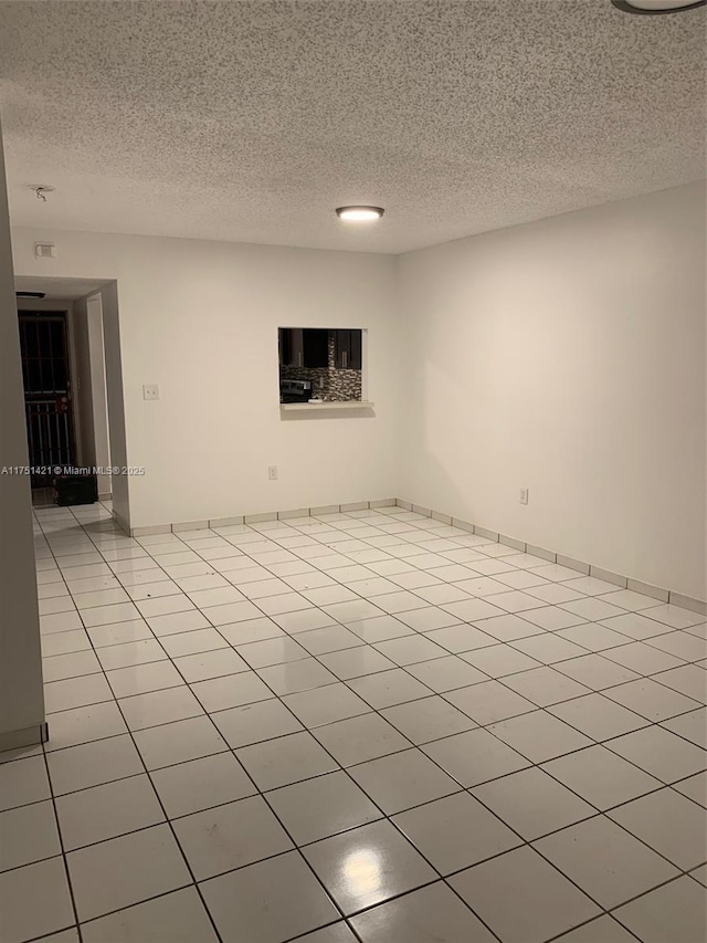 spare room with baseboards, a textured ceiling, and light tile patterned flooring