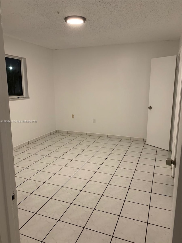 unfurnished room with a textured ceiling, light tile patterned floors, and baseboards