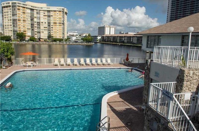 pool with a patio area, a water view, and fence