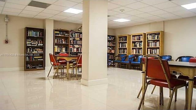 office area with wall of books, baseboards, and a drop ceiling