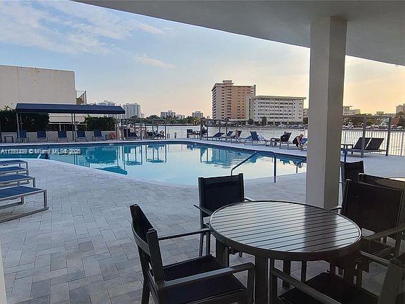 pool at dusk featuring a city view, a patio, a community pool, and fence