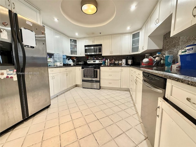 kitchen with appliances with stainless steel finishes, dark countertops, a raised ceiling, and white cabinets