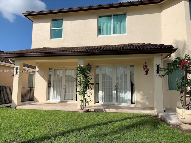 rear view of property featuring french doors, a lawn, and stucco siding