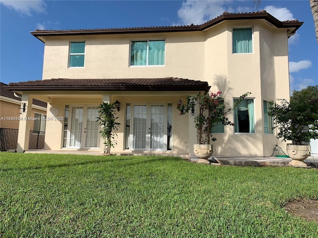 back of property with a lawn, french doors, and stucco siding