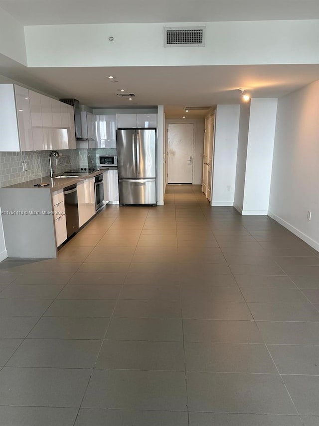 kitchen featuring visible vents, decorative backsplash, stainless steel appliances, wall chimney range hood, and white cabinetry