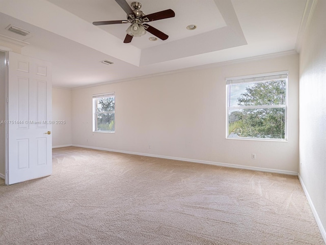 spare room featuring a tray ceiling, light colored carpet, visible vents, and baseboards