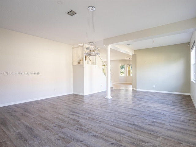 spare room featuring decorative columns, visible vents, wood finished floors, baseboards, and stairs