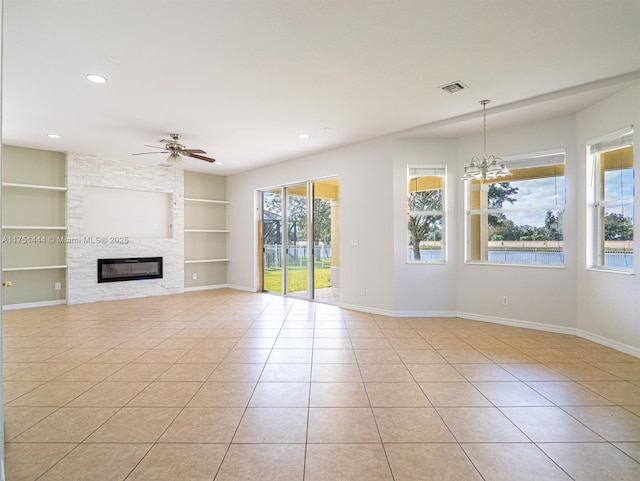 unfurnished living room with built in shelves, light tile patterned flooring, a large fireplace, ceiling fan with notable chandelier, and baseboards