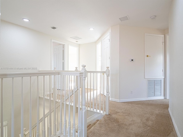 corridor with an upstairs landing, baseboards, visible vents, and carpet flooring