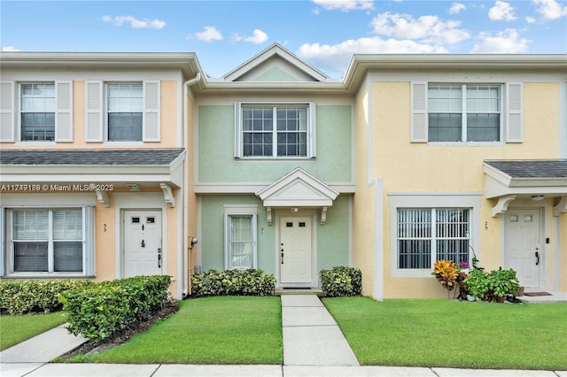 multi unit property with a shingled roof, a front lawn, and stucco siding