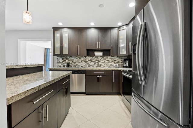 kitchen with light tile patterned floors, light stone counters, dark brown cabinetry, stainless steel appliances, and glass insert cabinets