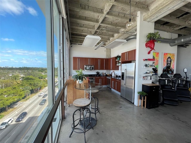 kitchen featuring reddish brown cabinets, modern cabinets, a high ceiling, stainless steel appliances, and concrete flooring