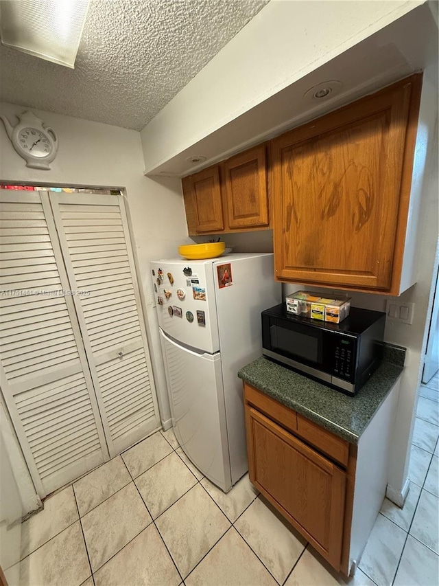 kitchen with brown cabinets, light tile patterned floors, dark countertops, freestanding refrigerator, and a textured ceiling