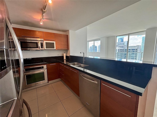 kitchen featuring brown cabinets, a sink, stainless steel appliances, light tile patterned floors, and a peninsula