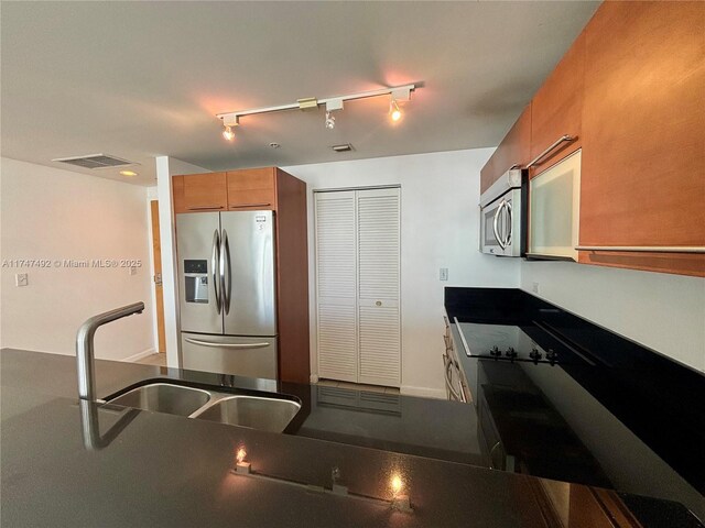 kitchen featuring stainless steel appliances, brown cabinets, dark countertops, a sink, and visible vents