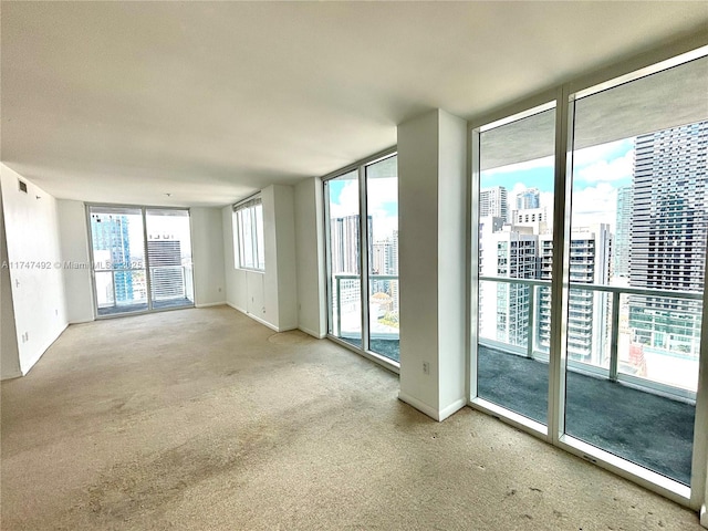 carpeted empty room featuring visible vents, a city view, and baseboards