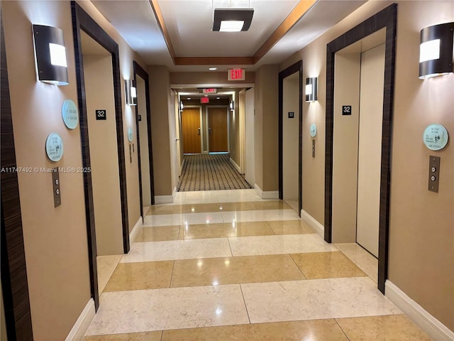 corridor with baseboards, light tile patterned floors, a raised ceiling, and elevator