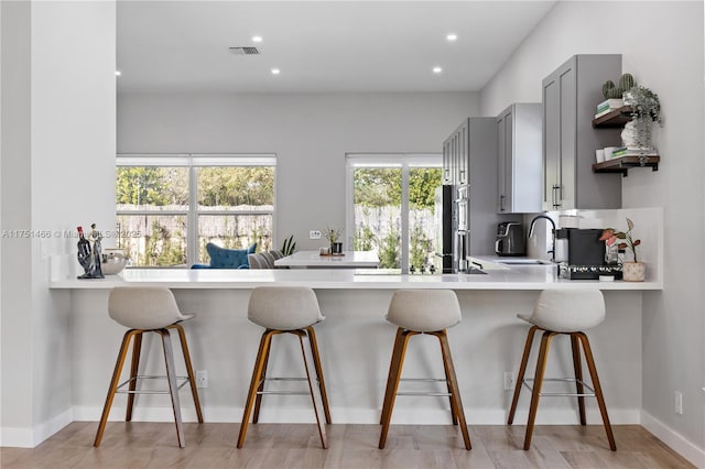 kitchen with a breakfast bar area, a peninsula, a sink, light countertops, and gray cabinets