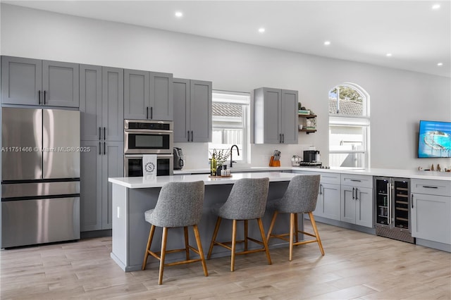 kitchen with beverage cooler, appliances with stainless steel finishes, a kitchen breakfast bar, a center island, and light countertops