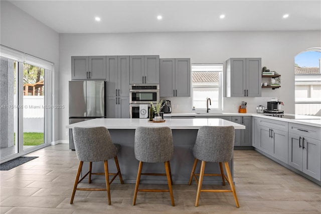 kitchen with appliances with stainless steel finishes, a breakfast bar, a center island, light countertops, and a sink