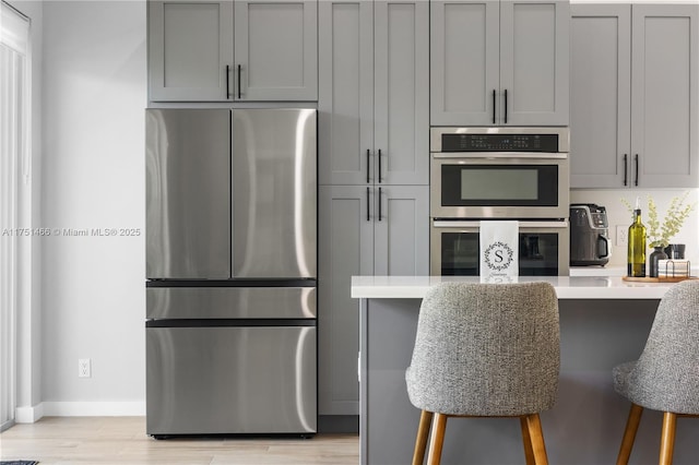 kitchen with gray cabinets, appliances with stainless steel finishes, light countertops, and a kitchen breakfast bar