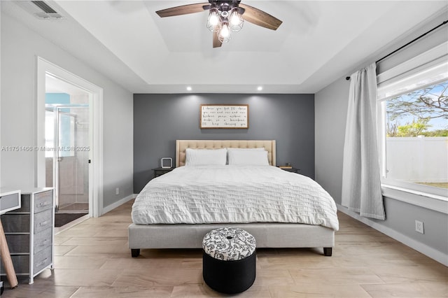 bedroom with ceiling fan, a tray ceiling, visible vents, and baseboards