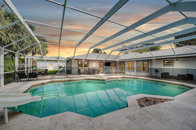 pool at dusk featuring glass enclosure, a water slide, a patio, and an outdoor pool