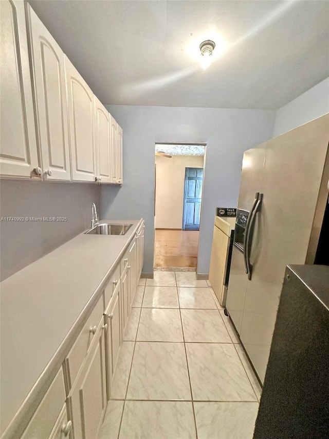 kitchen with light tile patterned floors, light countertops, white cabinetry, a sink, and white fridge with ice dispenser