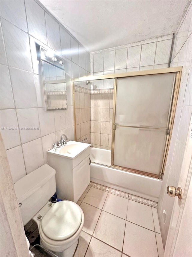 bathroom featuring tile patterned flooring, toilet, bath / shower combo with glass door, vanity, and tile walls