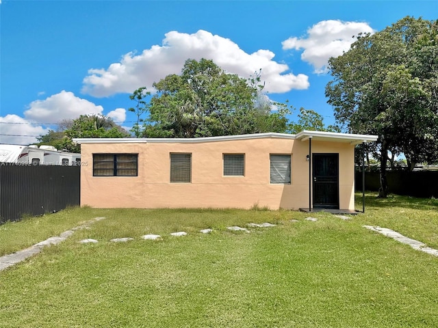 back of house with a lawn, fence, and stucco siding