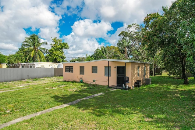 rear view of property with central air condition unit, a lawn, fence, and stucco siding