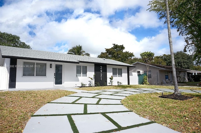 ranch-style home with a front lawn, roof with shingles, and stucco siding