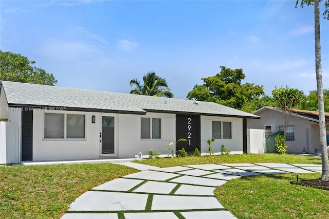 ranch-style home featuring a front lawn, a shingled roof, and stucco siding