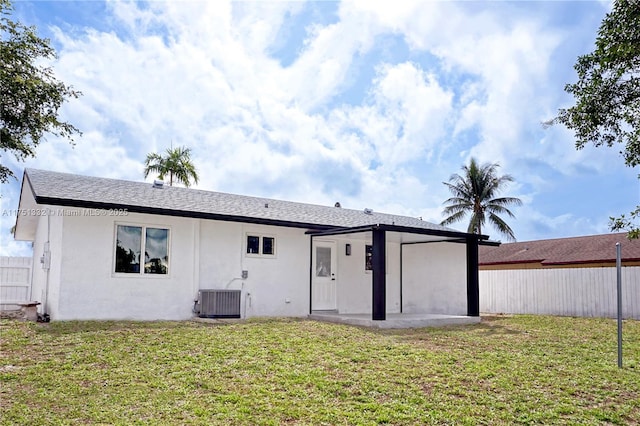 back of property with central AC unit, a shingled roof, fence, a yard, and stucco siding