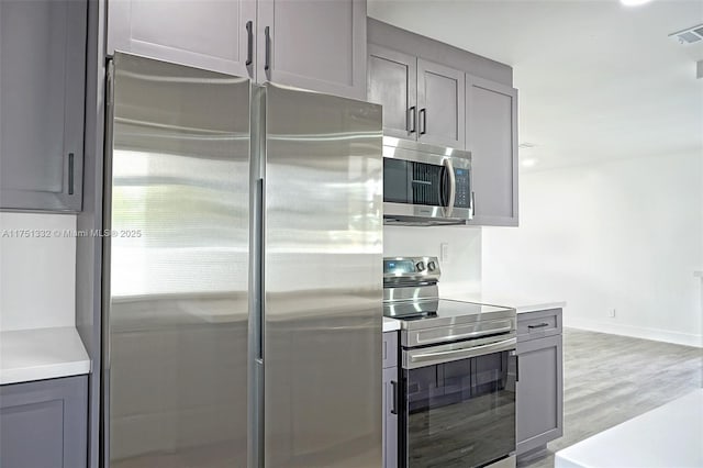 kitchen featuring stainless steel appliances, gray cabinetry, light wood-style flooring, light countertops, and baseboards