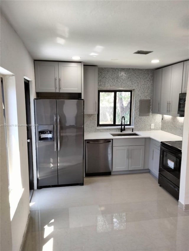 kitchen featuring appliances with stainless steel finishes, backsplash, a sink, and gray cabinetry