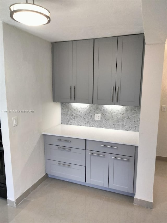 kitchen with baseboards, gray cabinets, backsplash, and light countertops