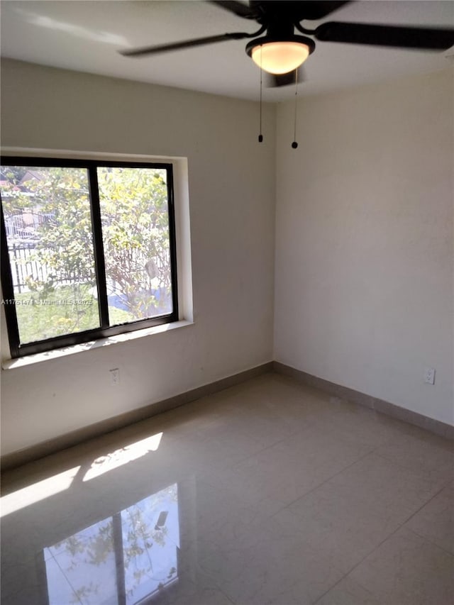 empty room with tile patterned flooring, a ceiling fan, and baseboards