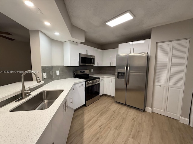 kitchen with stainless steel appliances, light stone counters, a sink, and white cabinets