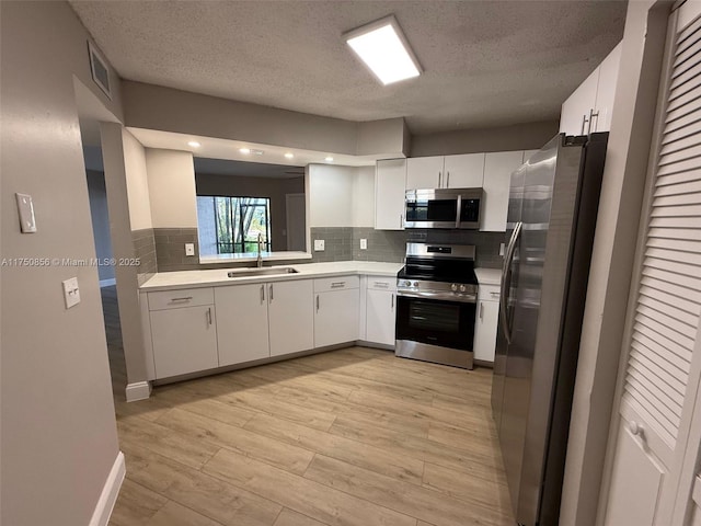 kitchen featuring stainless steel appliances, a sink, white cabinets, light countertops, and light wood finished floors