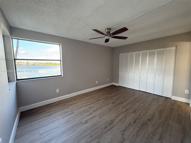 unfurnished bedroom featuring a textured ceiling, baseboards, and wood finished floors