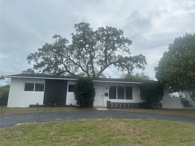 ranch-style home with driveway, a front lawn, and stucco siding