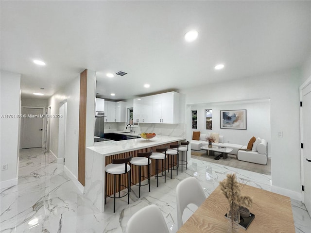 kitchen with a breakfast bar area, a peninsula, recessed lighting, white cabinets, and marble finish floor