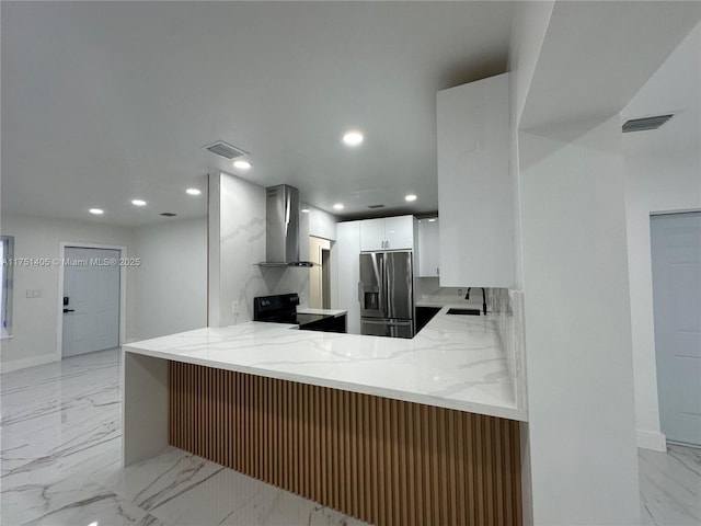 kitchen featuring wall chimney exhaust hood, a peninsula, white cabinetry, stainless steel refrigerator with ice dispenser, and a sink