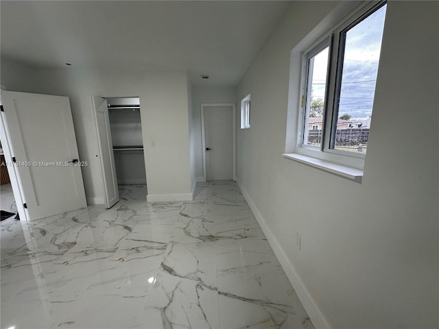 unfurnished bedroom with marble finish floor, a closet, and baseboards