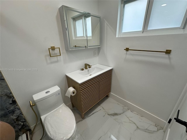 half bath with toilet, marble finish floor, baseboards, and vanity