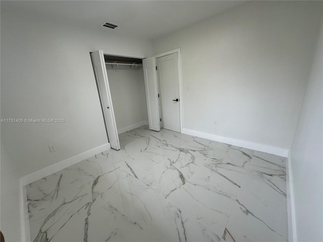 unfurnished bedroom featuring a closet, marble finish floor, visible vents, and baseboards