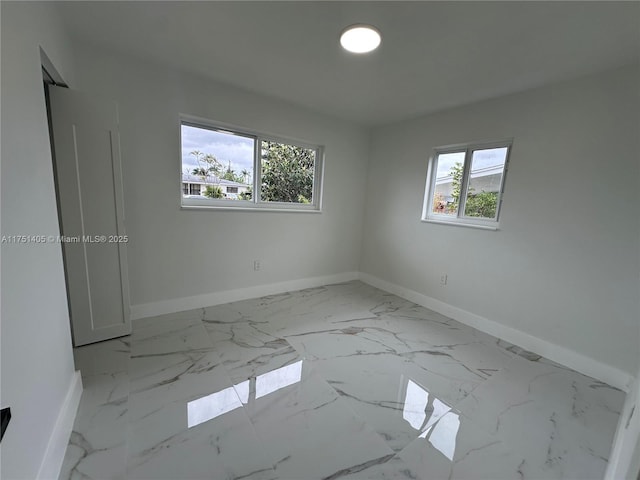 empty room with a healthy amount of sunlight, marble finish floor, and baseboards